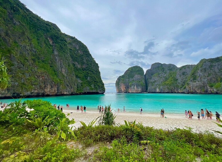 A beach with people, turquoise water, and green cliffs. 1