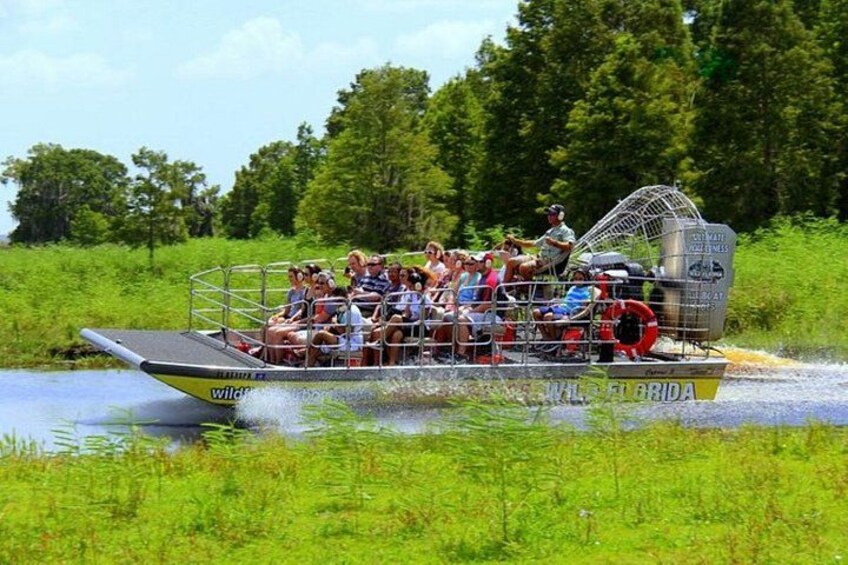 A boat with people on it, moving through water with greenery around. 5