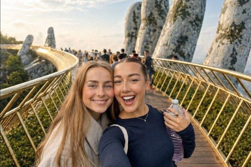 Two people taking a selfie on a bridge with large rock formations in the background. 1