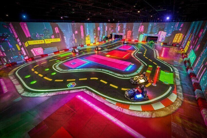 Eine hell erleuchtete, indoor Arena mit Rennbahn und farbenfrohen Projektionen an den Wänden. 1