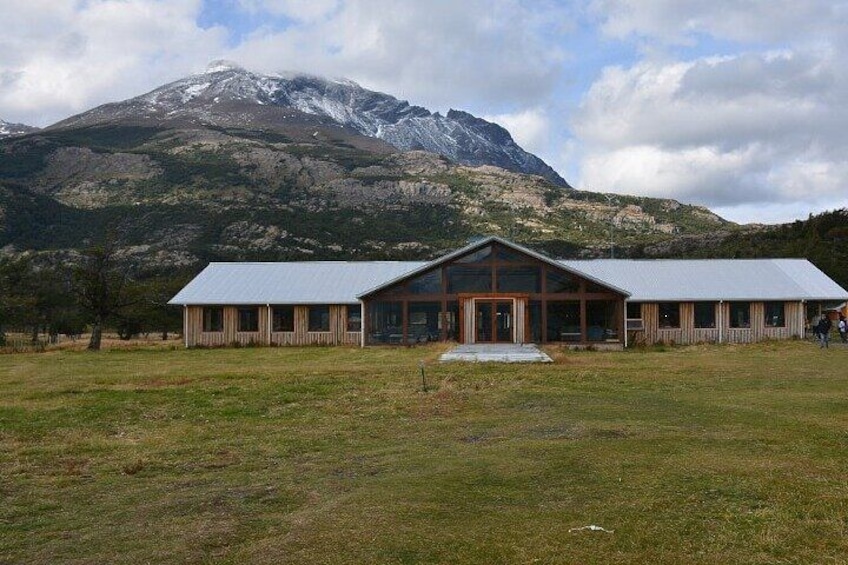 A building with a metal roof and wooden walls, surrounded by a grassy field and a mountain in the background. 3