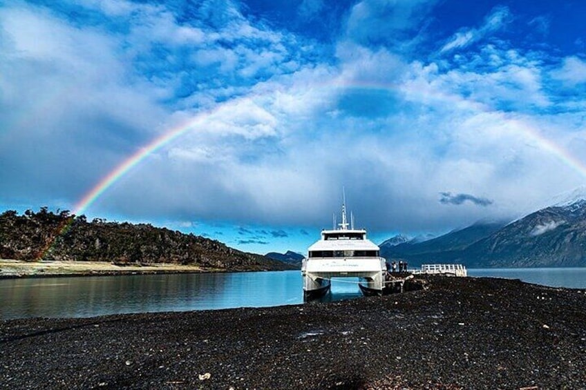 A boat on a beach with a rainbow and mountains in the background. 1