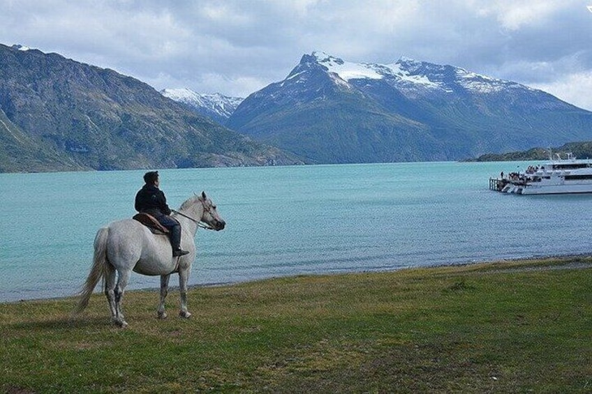A person riding a white horse by a lake with mountains in the background. 5