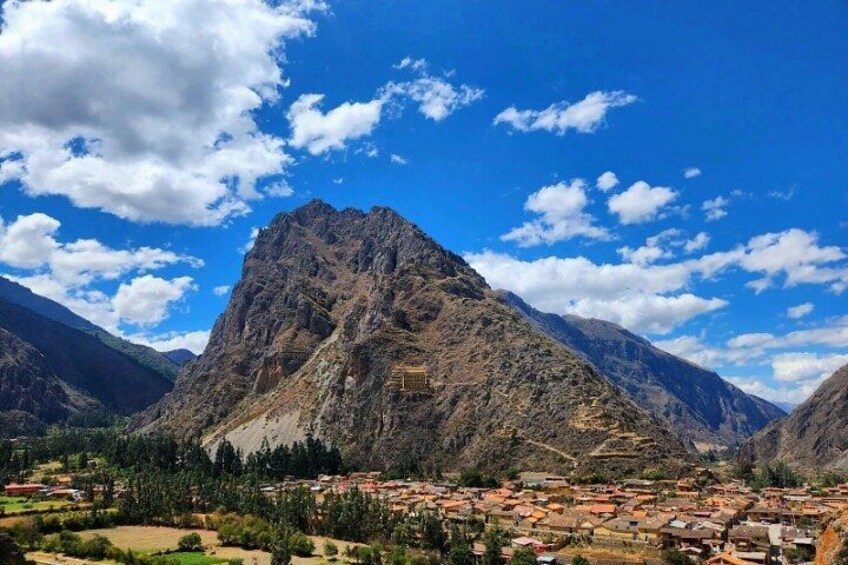 A mountainous landscape with a prominent peak, a valley with scattered buildings, and a clear blue sky with clouds. 2