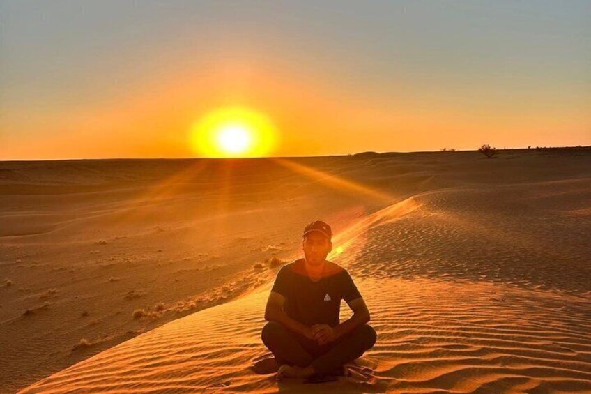 A person sitting on a sand dune at sunset. 1
