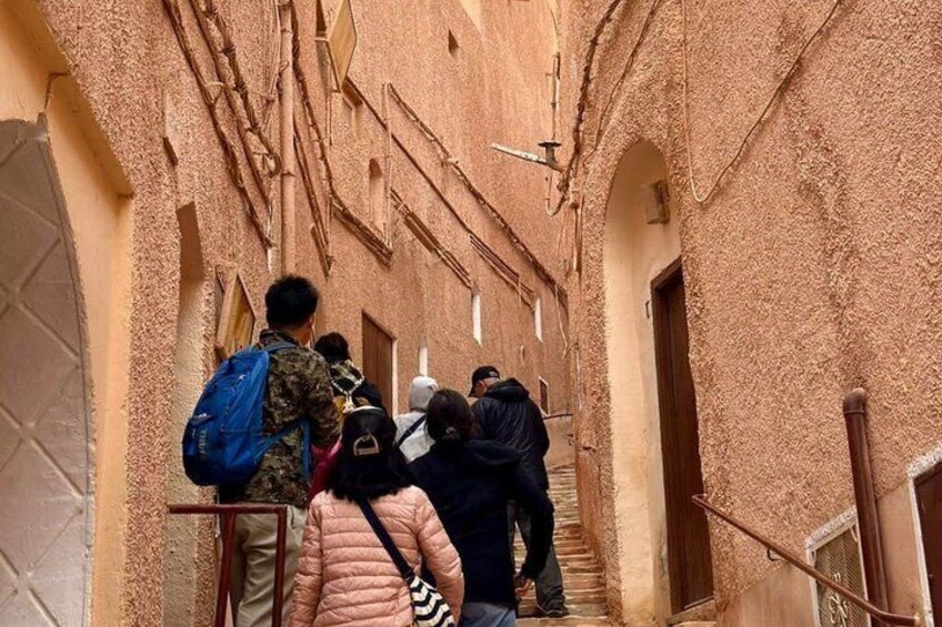 A narrow alley with people walking, textured walls, and arched doorways. 5