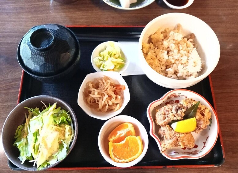 A traditional Japanese meal with rice, vegetables, and fish on a black tray. 3