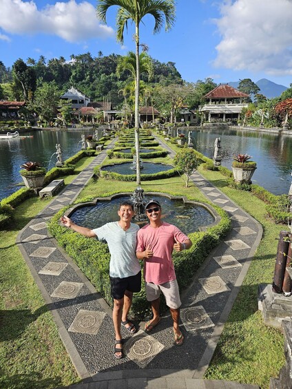 A man and woman standing on a patterned pathway beside a pond with statues and a palm tree in a landscaped garden. 4