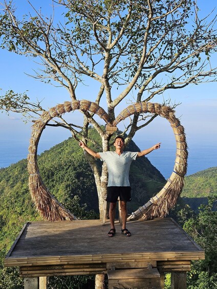 A person standing on a wooden platform with a heart-shaped structure made of branches and leaves. 3