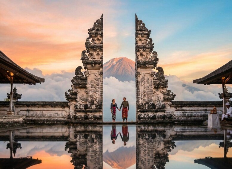 A couple holding hands in front of ancient stone gates with a mountain in the background. 1