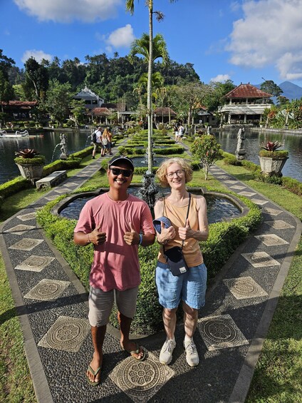 A couple standing on a patterned walkway with a water feature and palm trees in the background. 5