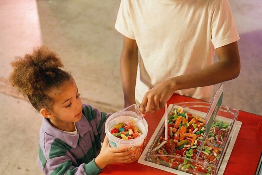 A child holding a container of candy, a tray of assorted candies, and a person standing behind them. 5