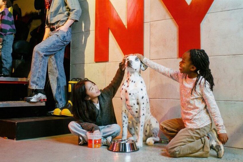 Two children interacting with a Dalmatian dog in front of a large red 'NY' sign. 4