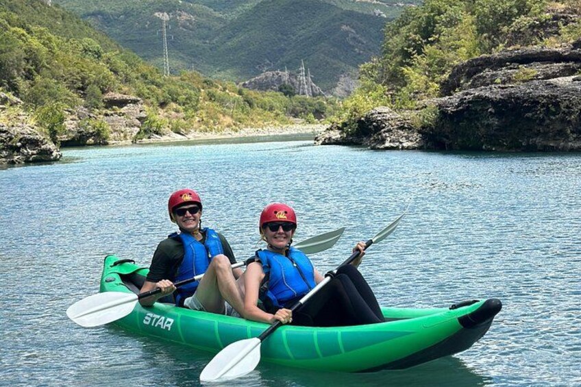 Two people kayaking on a river surrounded by greenery and hills. 4