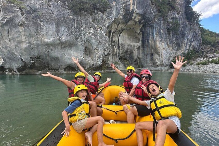 A group of people on a yellow raft with life jackets, surrounded by rocky cliffs and calm water. 3