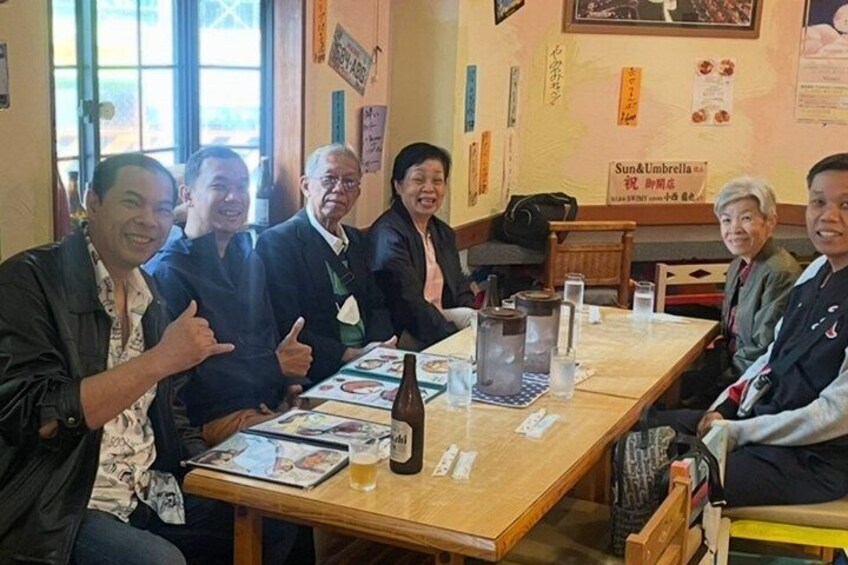 A group of people sitting around a wooden table with a bottle and glasses on it. 1
