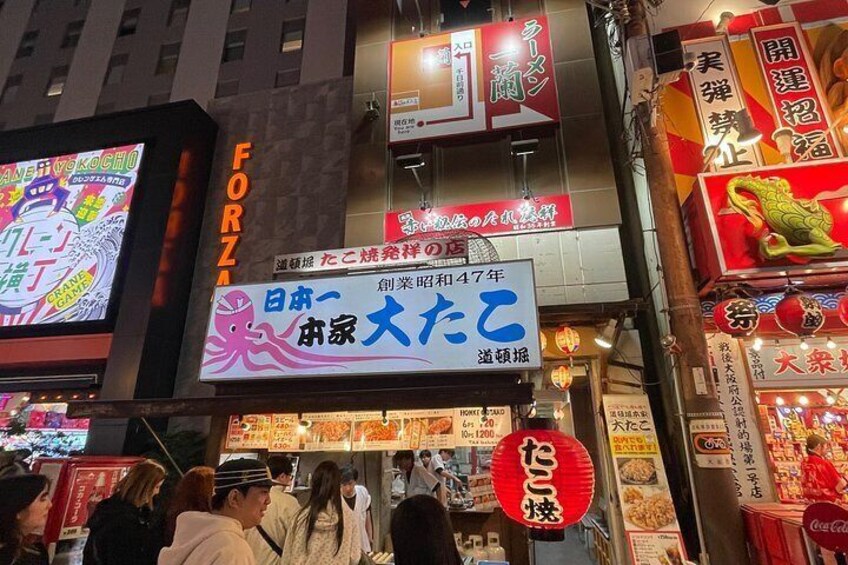 A busy street with illuminated signs and storefronts, including a prominent red and white sign with Japanese characters. 5