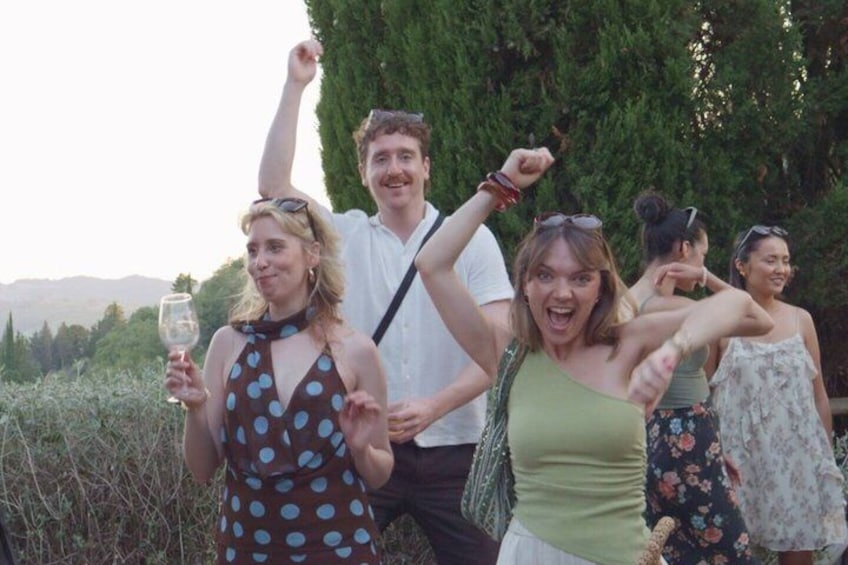 A group of people outdoors, some holding drinks, with trees and a mountainous background. 2