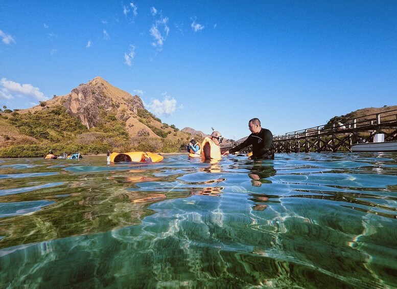 A person in a wetsuit assisting another in a kayak on a clear waterway with a mountain in the background. 4