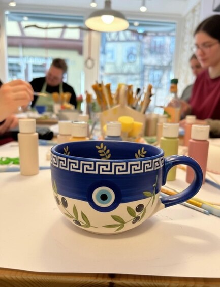 A blue mug with a decorative pattern and a handle, placed on a table with various items around it. 1