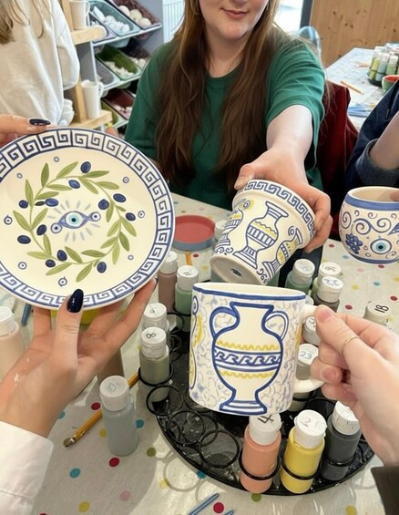 People engaged in pottery making, holding decorated ceramic plates and mugs. 2