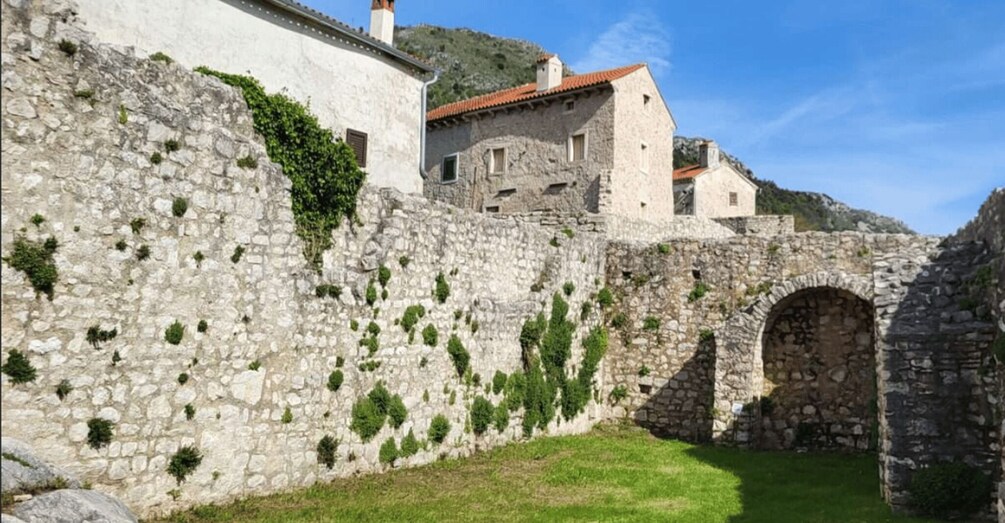 A stone wall with a grassy area and a building with a red roof. 5