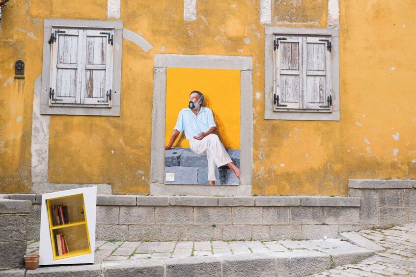 A mural of a man sitting on steps, a yellow wall, and a white bookshelf. 4