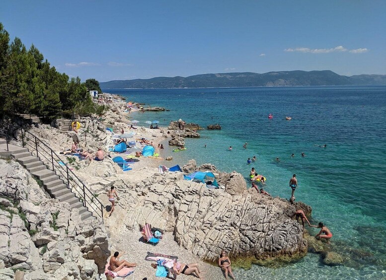 A rocky beach with clear water, people sunbathing, and a staircase leading down to the shore. 2