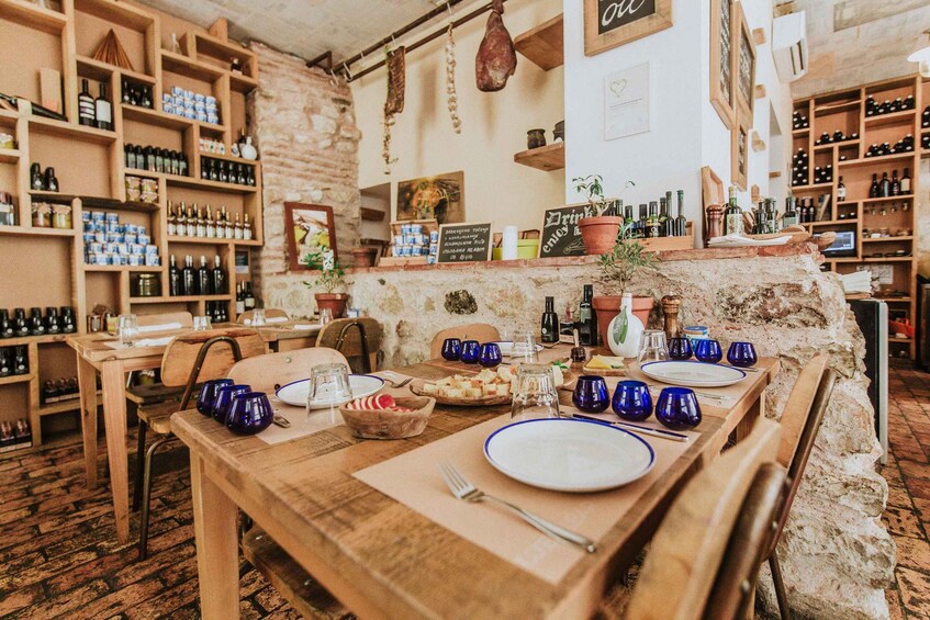 A rustic restaurant interior with wooden tables, blue glassware, and shelves of wine bottles. 1