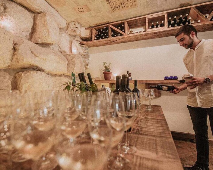 A wine cellar with a wooden table filled with wine glasses, a wine rack, and a person pouring wine. 3