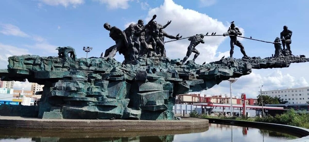 A bronze statue of soldiers on a rocky outcrop above a reflective water surface. 1