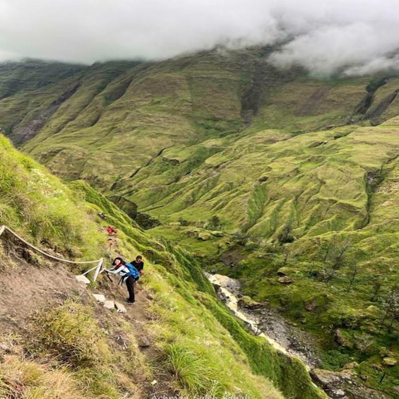 A hiker on a steep, grassy mountain trail with a rope for safety. 2