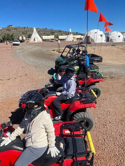 A group of people on ATVs in a dry, rocky area with tents and a hill in the background. 2