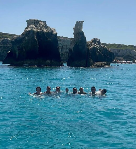 People swimming in a clear blue sea with rocky formations in the background. 2