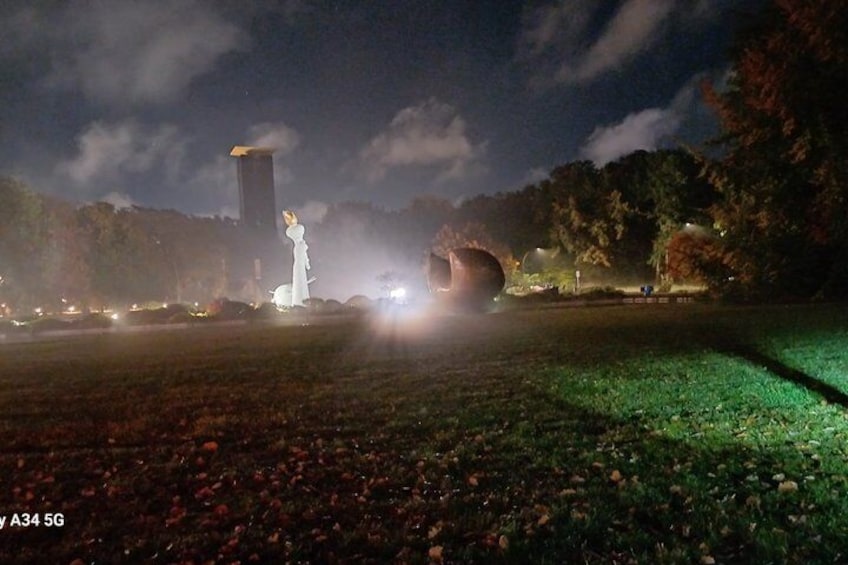 Escena nocturna con una estatua iluminada por luces, una estructura grande que recuerda a una torre, y la entrada de un túnel. 1