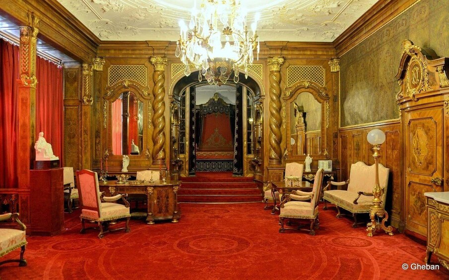 An opulent room with ornate furniture, a grand chandelier, and a red carpet. 3