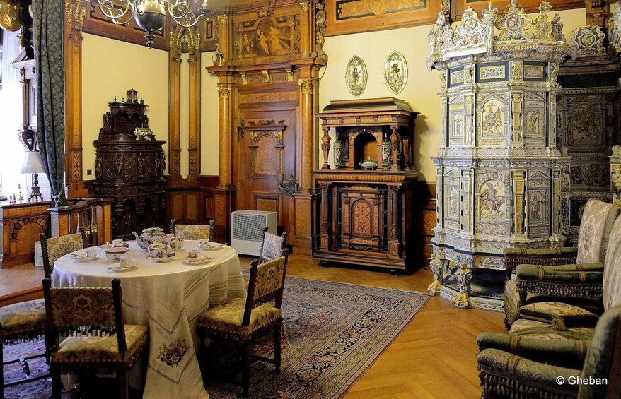 An ornate room with a round table set for a meal, surrounded by antique furniture and a large, intricately carved cabinet. 4