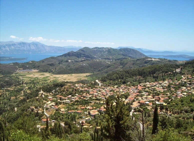 A coastal town with red-roofed houses, surrounded by green hills and mountains, with a clear blue sky. 3