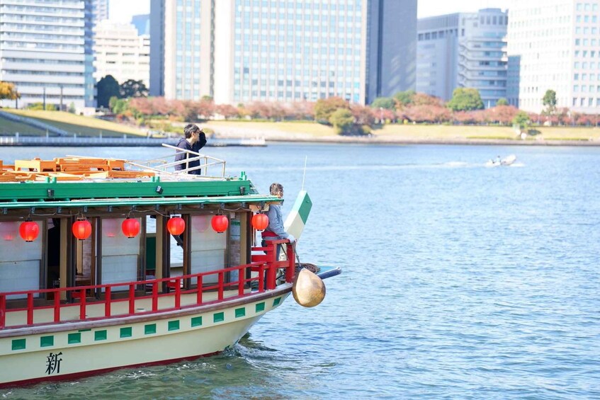 A traditional boat with red lanterns and a green and white color scheme on a river, with a cityscape in the background. 1