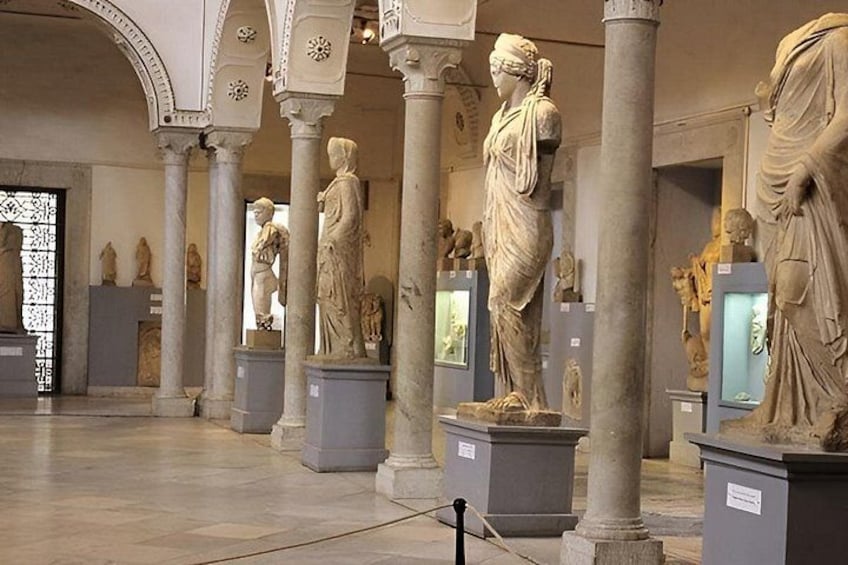 Een museuminterieur met klassieke beelden op sokkels, zuilen en bogen. 2