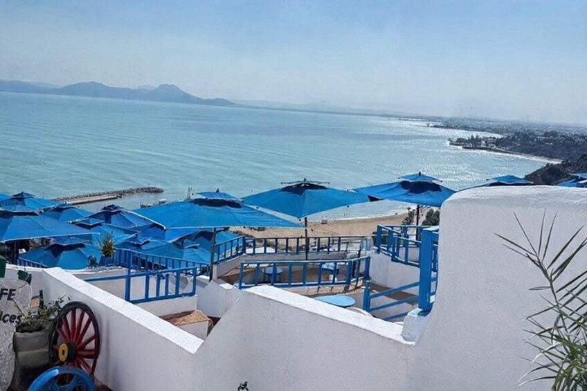 Een terras aan zee met blauwe parasols, witte muren en uitzicht op de oceaan. 1