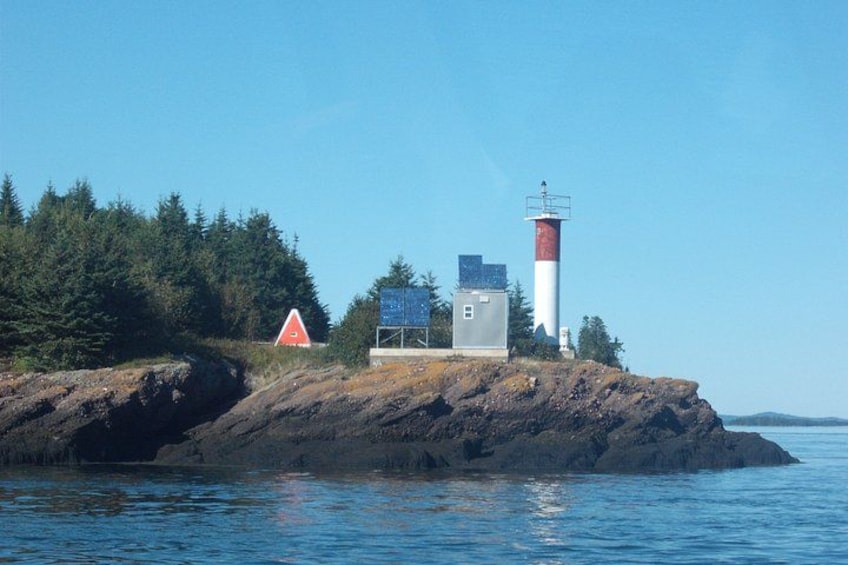 A lighthouse on a rocky island with a red and white structure nearby. 4