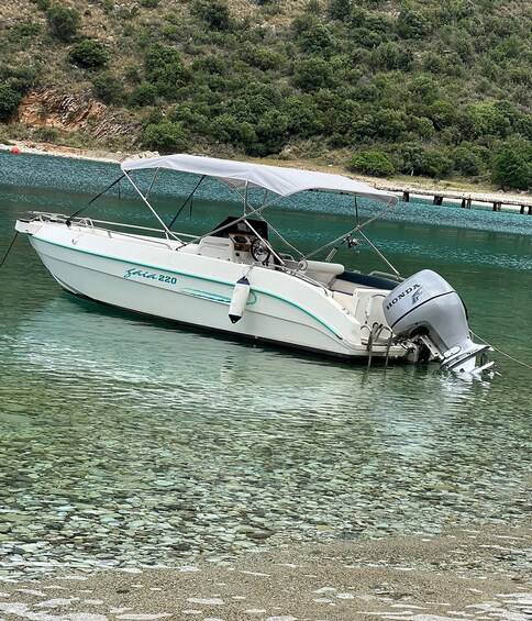 A white boat named 'saina220' docked at a rocky shore with clear water. 2