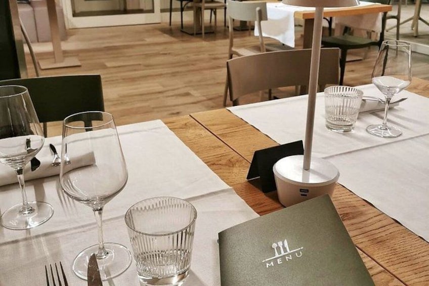 A restaurant table set with wine glasses, a menu, and a candle holder. 3