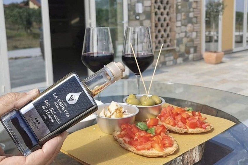 A person pouring a bottle of wine into a glass, with a table setting that includes a plate of food and two glasses of red wine. 4