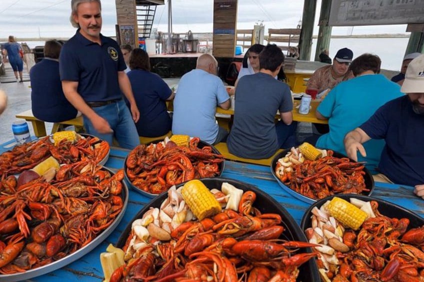 A group of people dining at a table with seafood, including lobsters and corn on the cob. 3