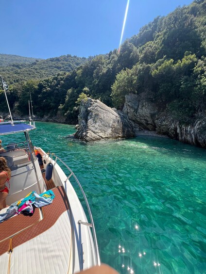 A boat on clear turquoise water with rocky cliffs and dense greenery in the background. 4