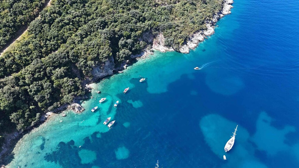 An aerial view of a coastal area with clear turquoise waters, rocky cliffs, and several boats anchored near the shore. 2