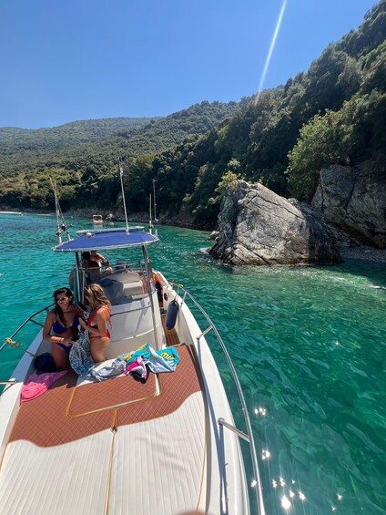 A boat with two people on deck, clear turquoise water, and a rocky coastline with greenery. 5