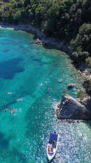 A clear turquoise sea with people swimming and a boat anchored near a rocky shore. 3
